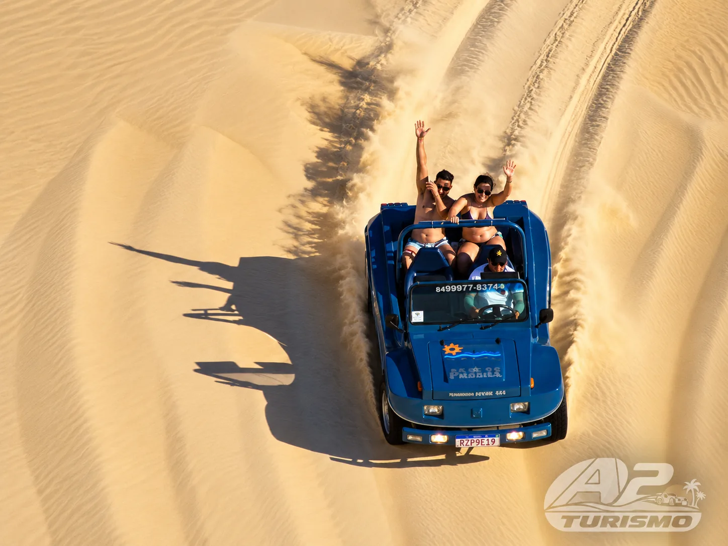 Vista de cima de um buggy azul seguindo trilhas na areia